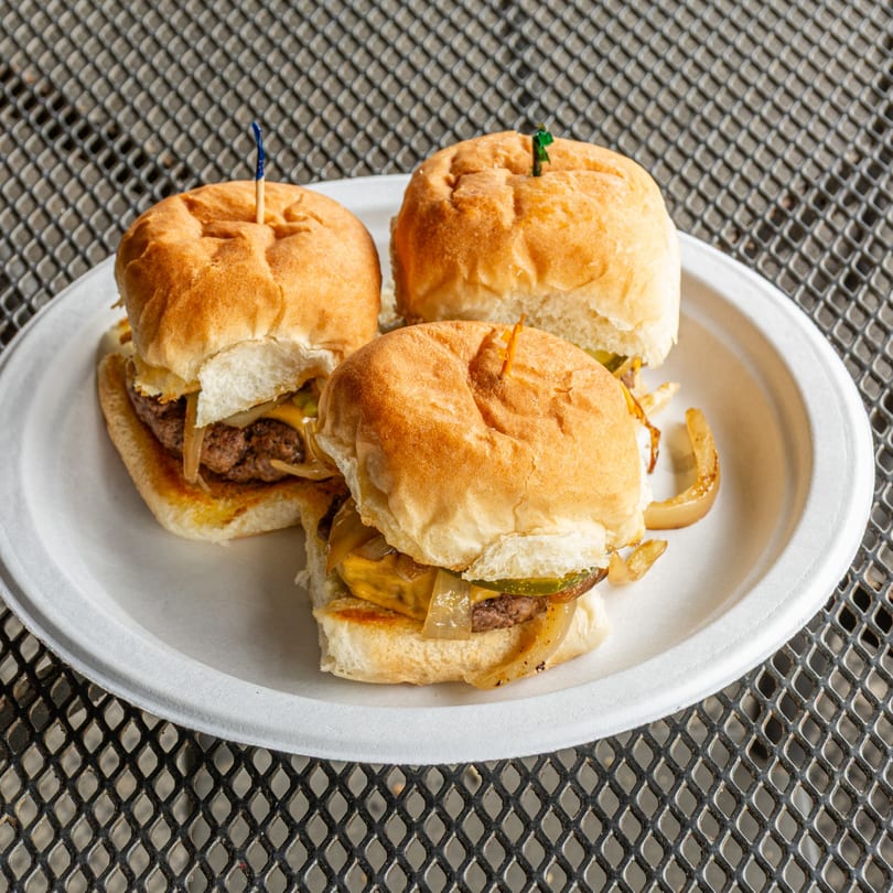 Three Jefferson Street Pub sliders with cheese, grilled onions, and pickles on a white plate.