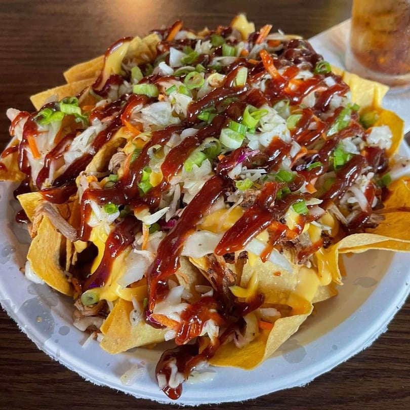 Pulled pork nachos with cheese, coleslaw, green onions, and BBQ sauce on a white plate.