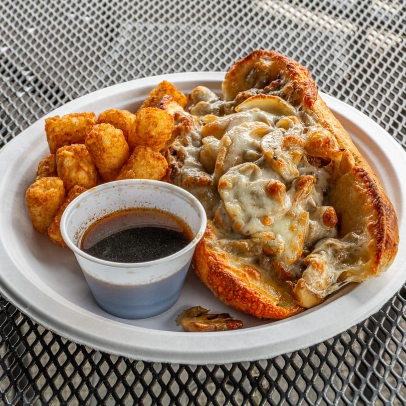 A Jefferson Street Pub cheesesteak with melted cheese and mushrooms, tater tots, and a side of au jus.