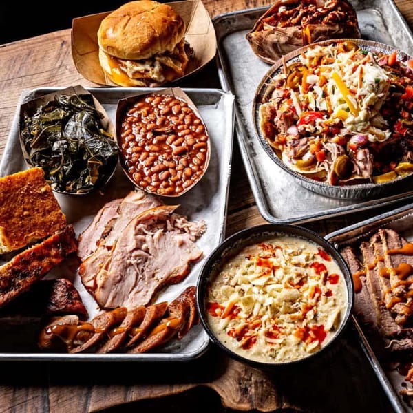 A feast of BBQ dishes, including ribs, sliced meats, baked beans, collard greens, and mac and cheese.