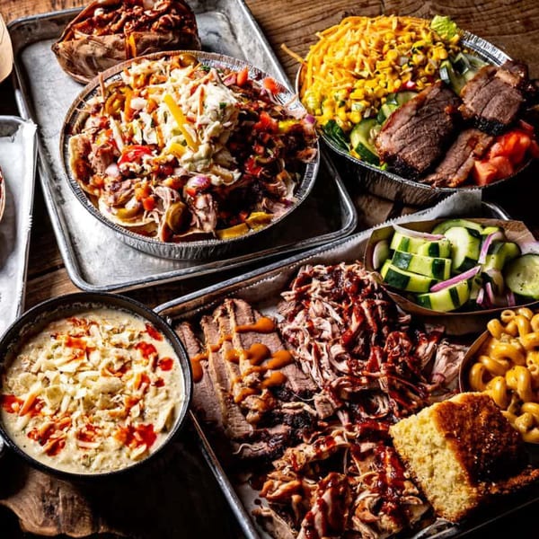 A feast of BBQ dishes, including pulled pork, brisket, mac and cheese, and cornbread.