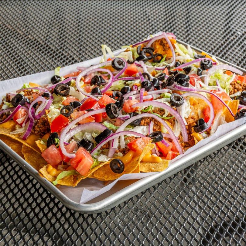 A large platter of Jefferson Street Pub nachos with ground beef, cheese, lettuce, tomatoes, red onions, and black olives.