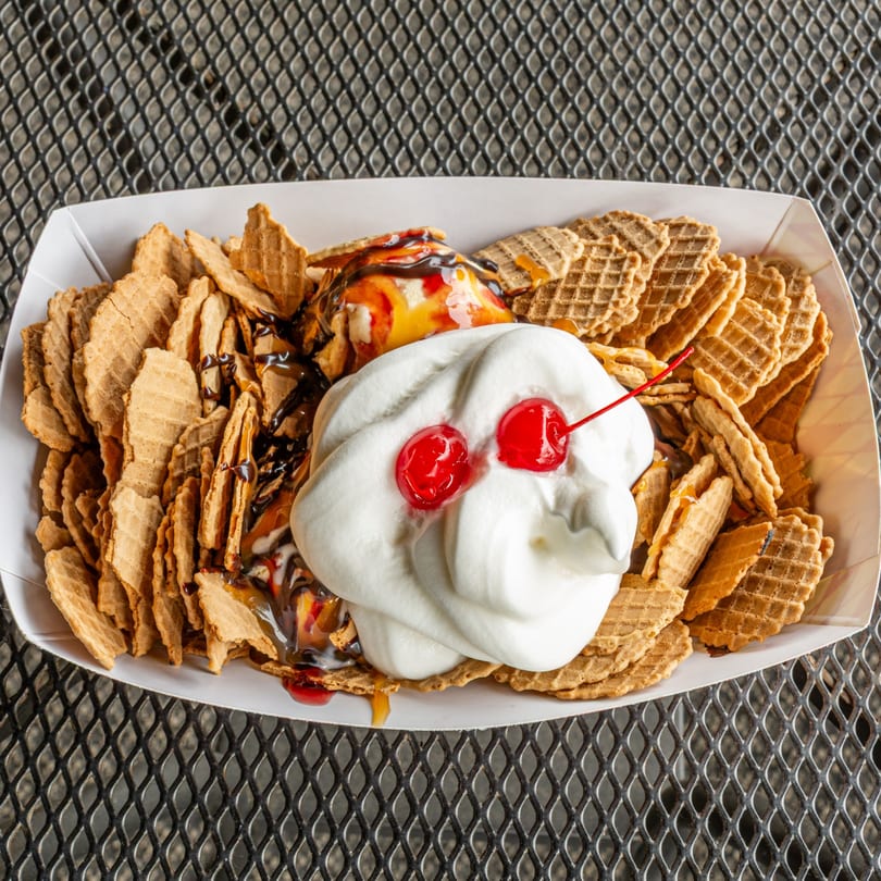 Waffle cone nachos with ice cream, whipped cream, cherries, and chocolate sauce in a white tray.